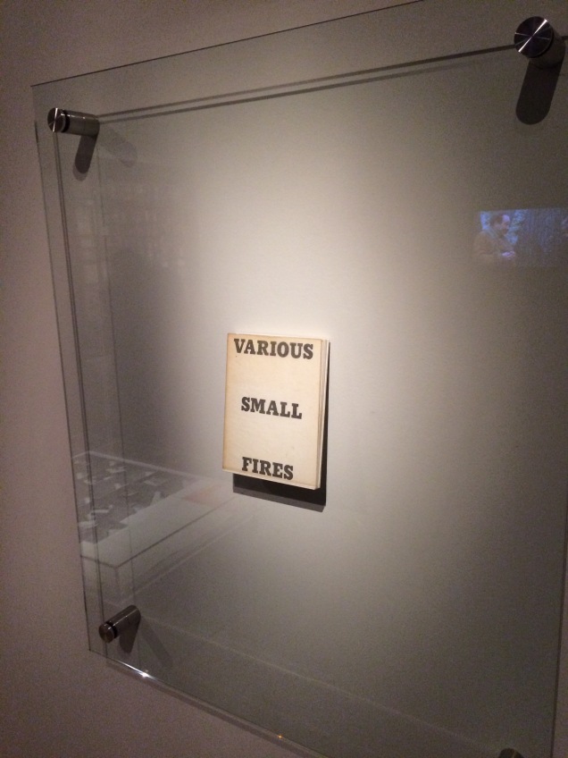 Display of Ed Ruscha's Various Small Fires and Milk, 1964, at Pliure: La Part du Feu, 2 February - 12 April 2015, Paris. Photo by Robert Bolick. Reflected in the lower left hand corner is the display of Bruce Nauman's Burning Small Fires; in the upper right corner, the film clip of Truffaut's 1966 Fahrenheit 451; and in the upper left, Maria Helena Vieira da Silva's La bibliotheque en feu, 1974.