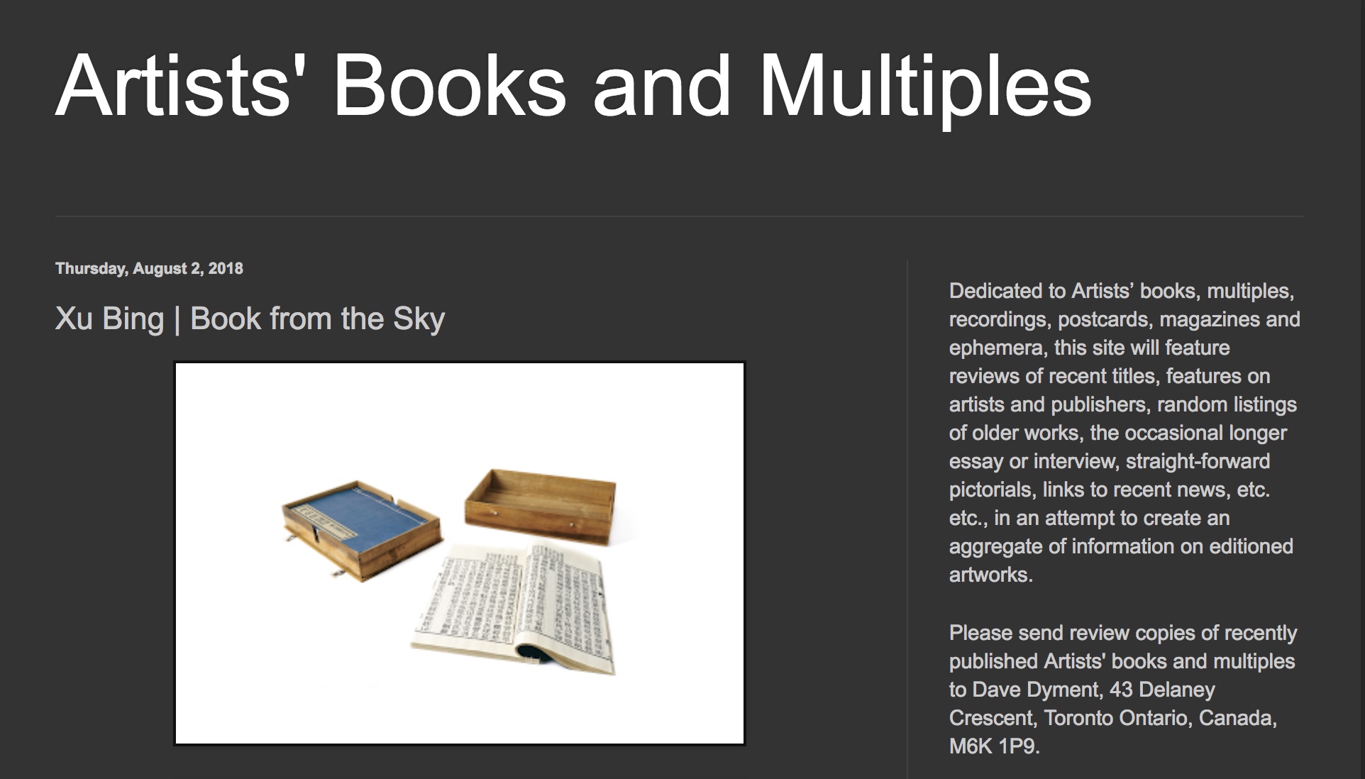 An artistic installation by Xu Bing titled 'Book from the Sky,' featuring an open book with text and two wooden boxes beside it. The background is plain white.