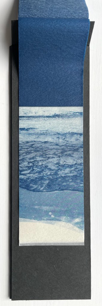 An artistic depiction of the ocean featuring various shades of blue paper, layered to create a textured landscape of waves and shoreline.