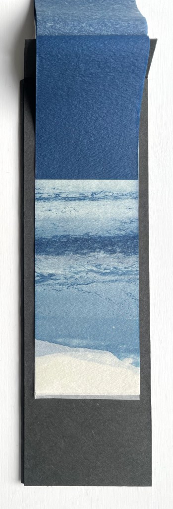 Vertical layout of a paper bookmark featuring a gradient of blue ocean waves and sandy shore, placed over a black background.