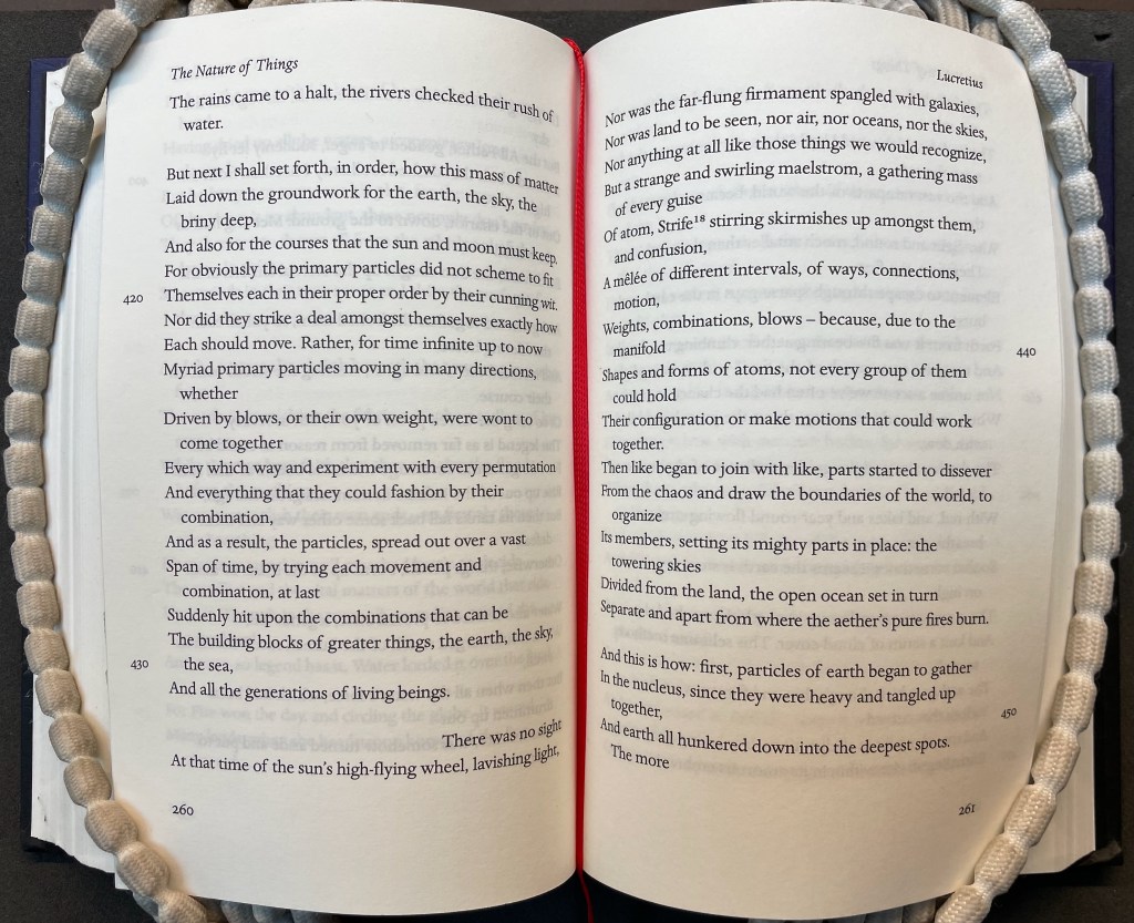 An open book displaying text from Lucretius' 'De Rerum Natura', highlighting themes of cosmic formation and the gathering of particles, with a decorative beaded bookmark along the edge.