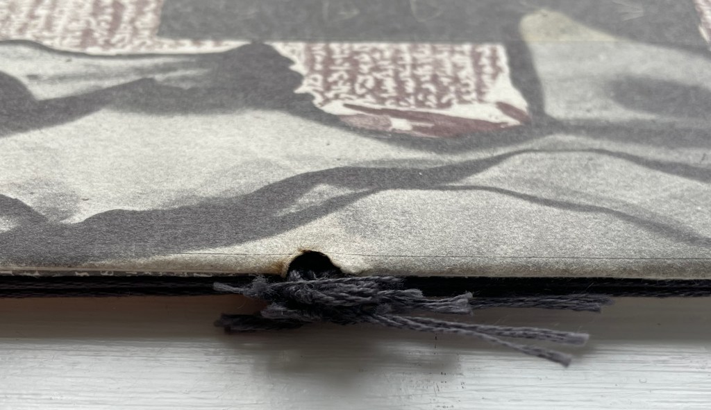 Close-up of the edge of a textured book, showing a hole with black threads tied in a bow.