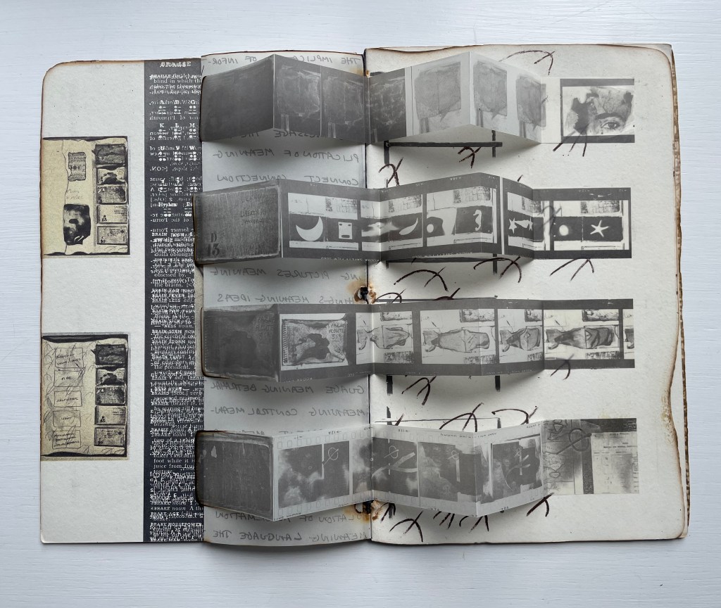 Open book with a fold-out section displaying black and white images and sketches, alongside handwritten notes and a dark background.