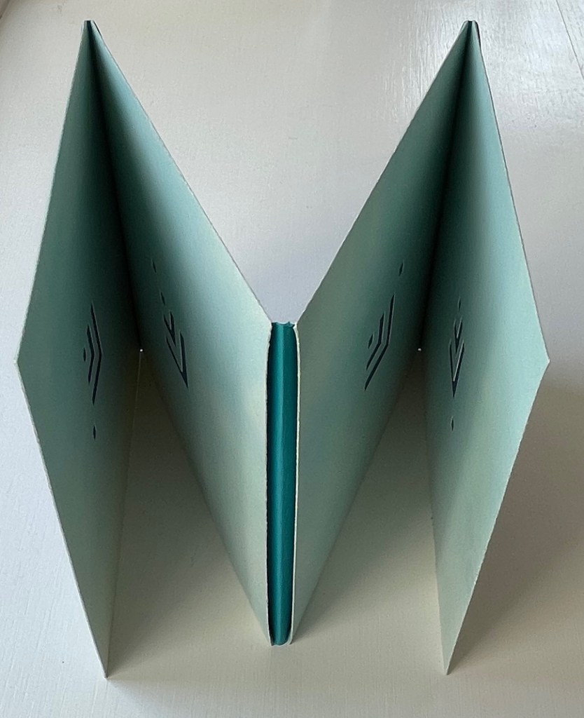 An open view of a light blue accordion booklet with decorative cut-out patterns on its panels, resting on a white surface.