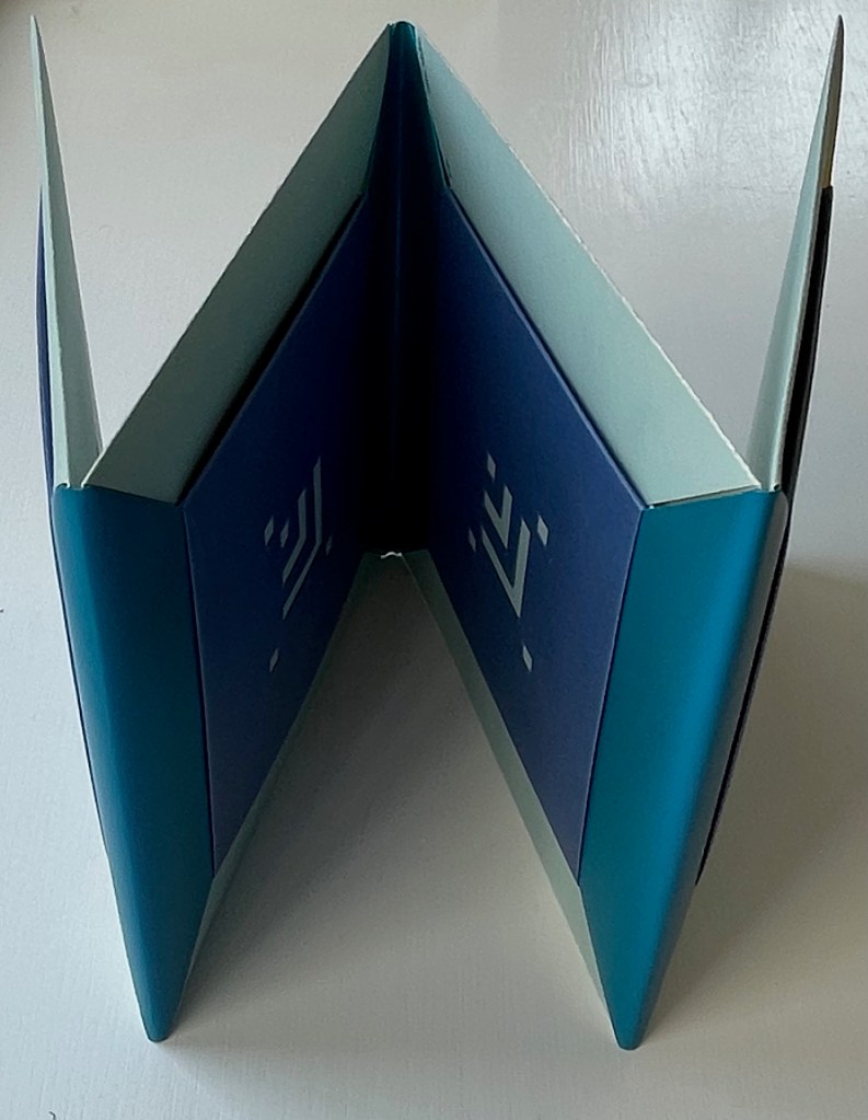 A close-up view of an open, colorful accordion book displaying layered blue and green panels, showcasing intricate designs on its interior.