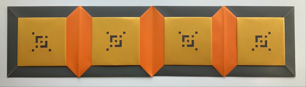 A horizontal arrangement of a multi-panel book with geometric patterns in yellow and orange, bordered by dark grey edges. The central panels feature repeated square motifs.