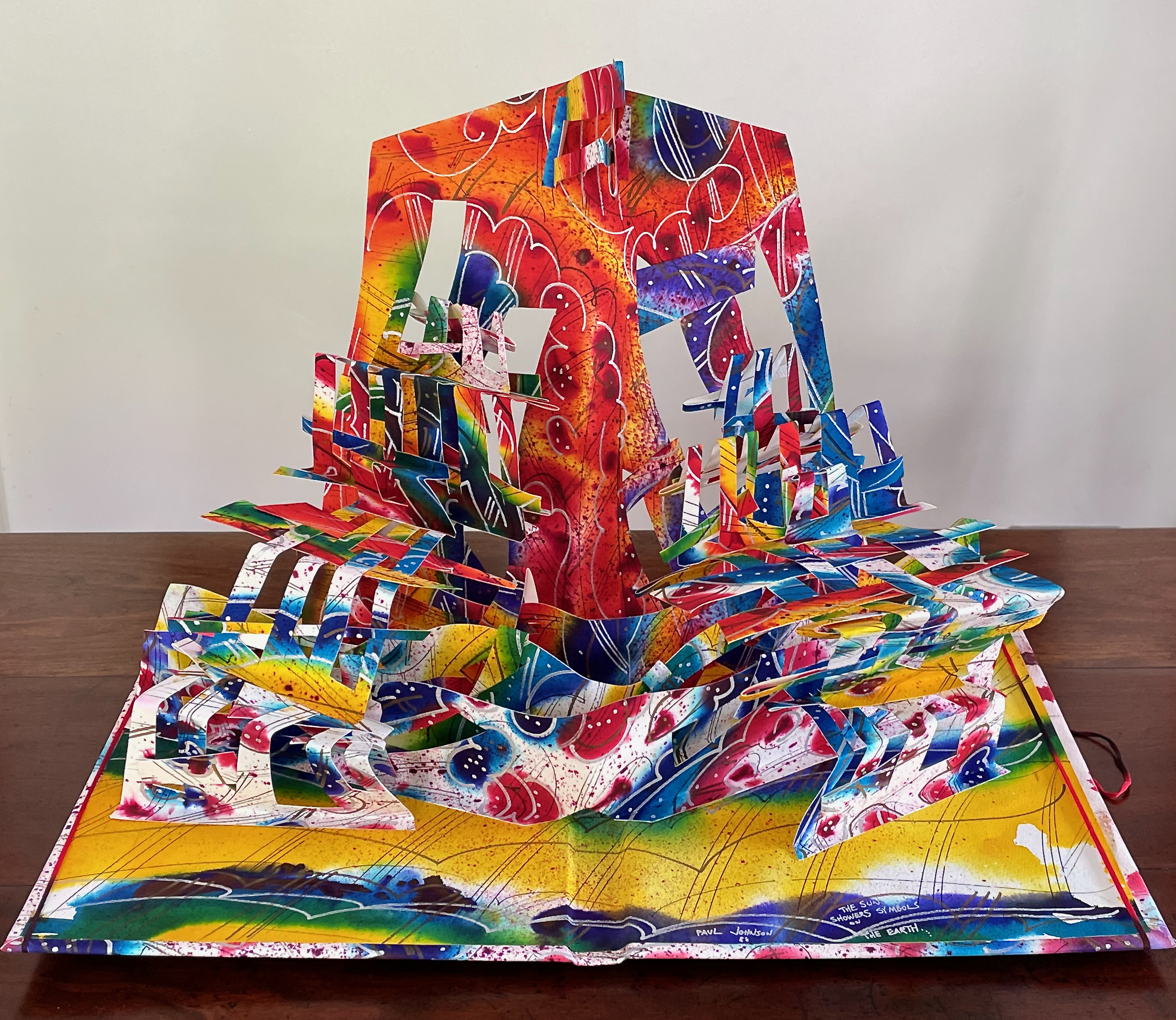 A colorful pop-up book featuring a vibrant three-dimensional landscape with abstract shapes and patterns, showcasing various layers of artistic design in a kaleidoscope of colors.