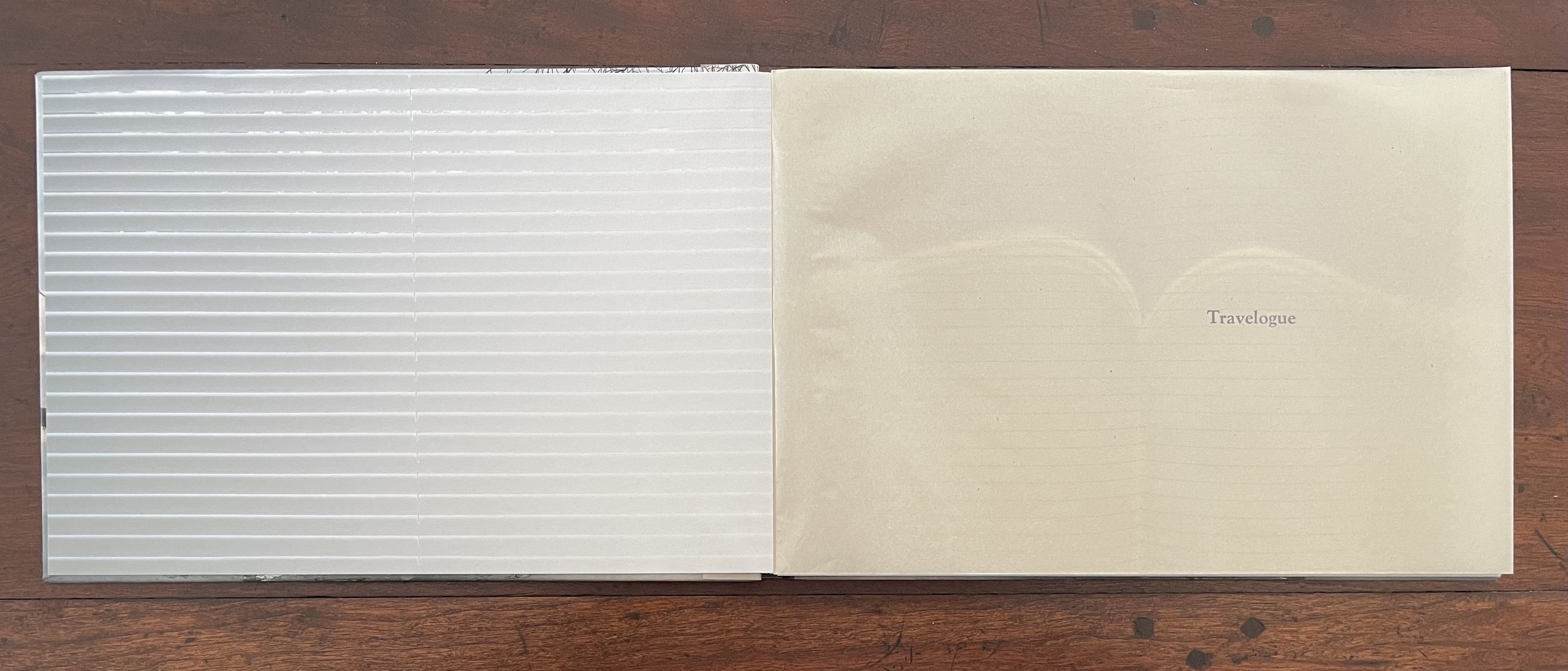 An open artist's book featuring a folded translucent cover on the left and a blank page with the title 'Travelogue' printed on the right.
