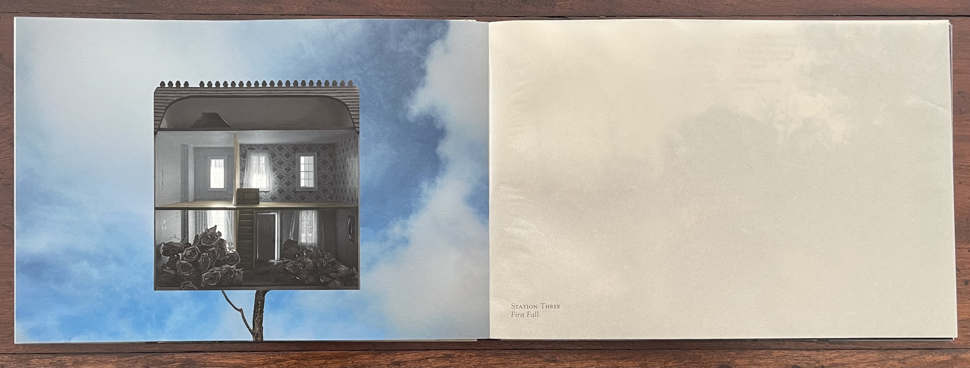 A digitally manipulated image of a dollhouse set against a blue sky, with a view of the interior. The scene features black roses in the foreground and highlights a first fall theme.