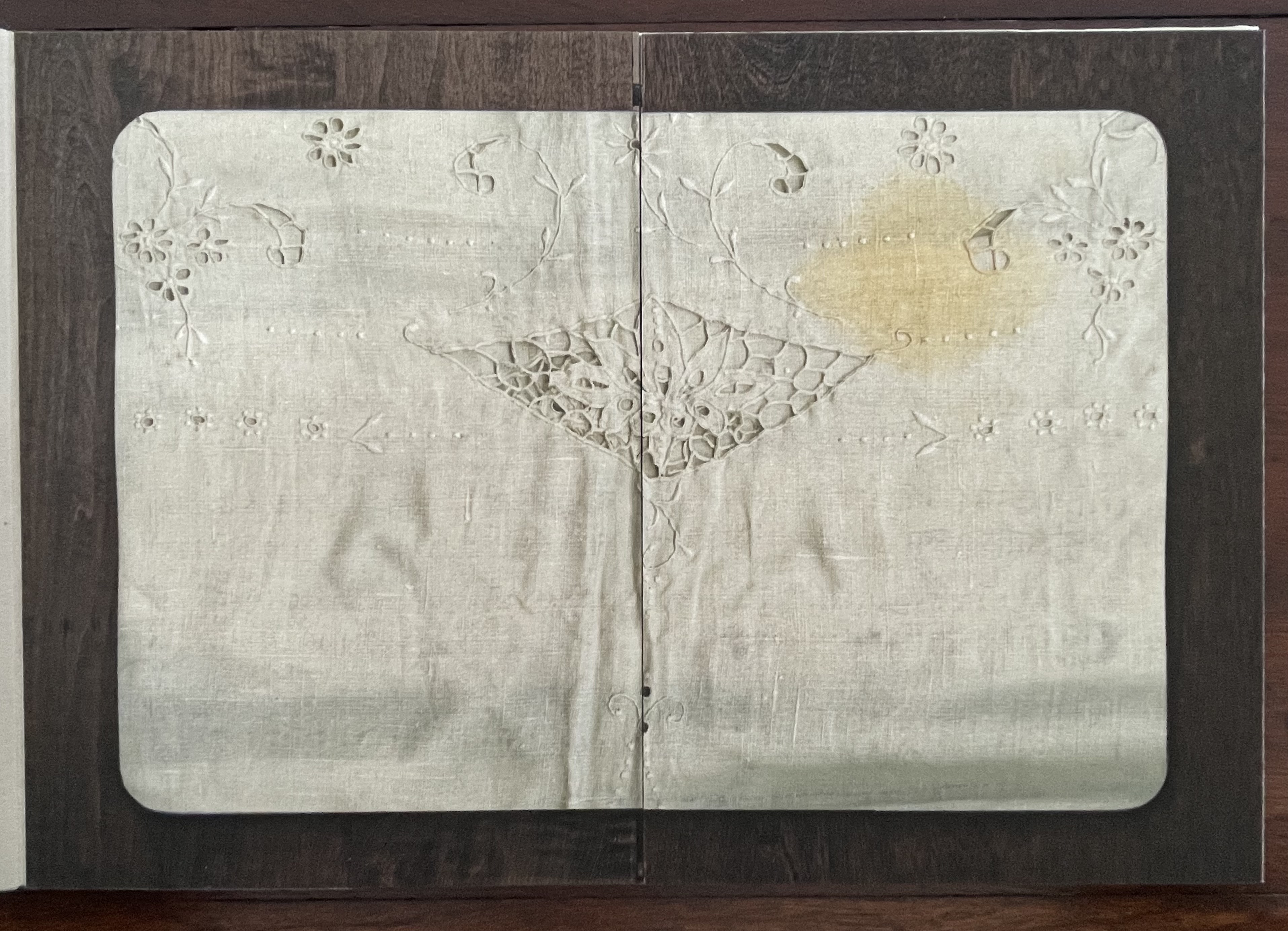 Open artist's book featuring intricate embroidered designs on a textured surface, including floral patterns and geometric motifs.