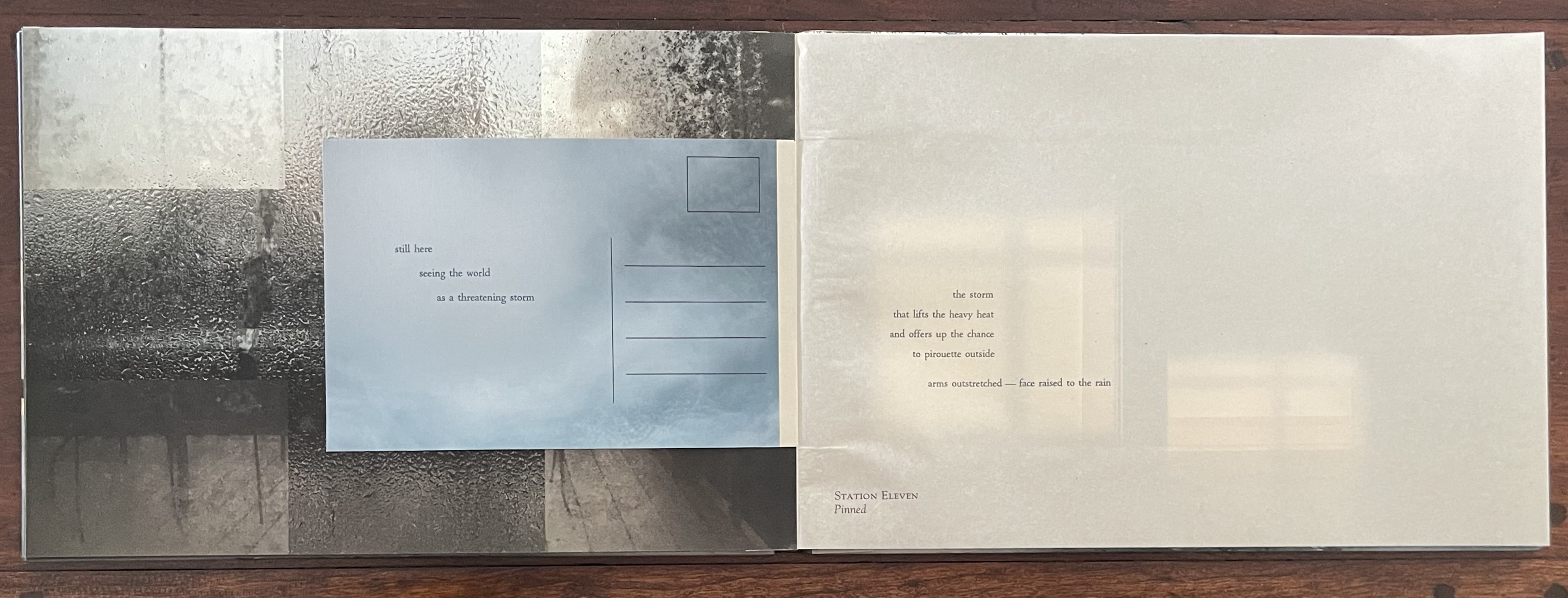 Open artist's book by Marlene MacCallum, displaying a textured cover with abstract patterns behind a foggy window, accompanied by minimalist text on blue paper, creating a contemplative visual and literary experience.