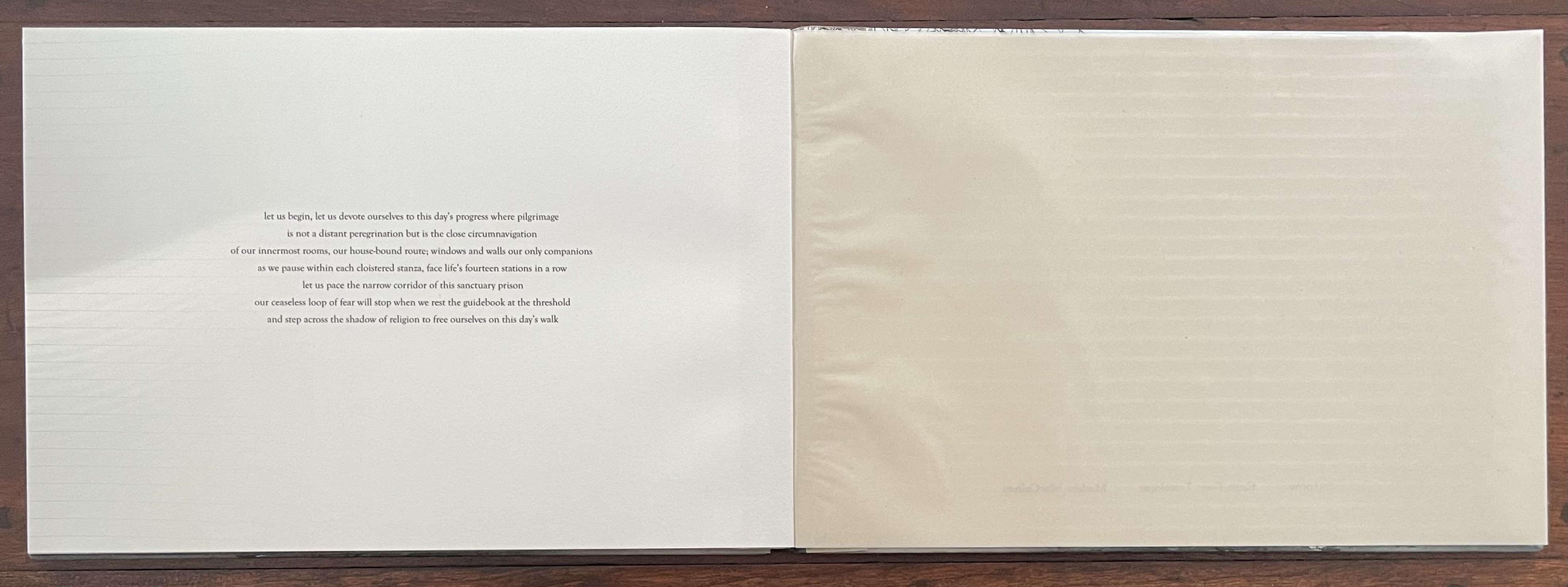 An open artist's book featuring text arranged on the left page, and a blank right page with a slight sheen, resting on a wooden surface.