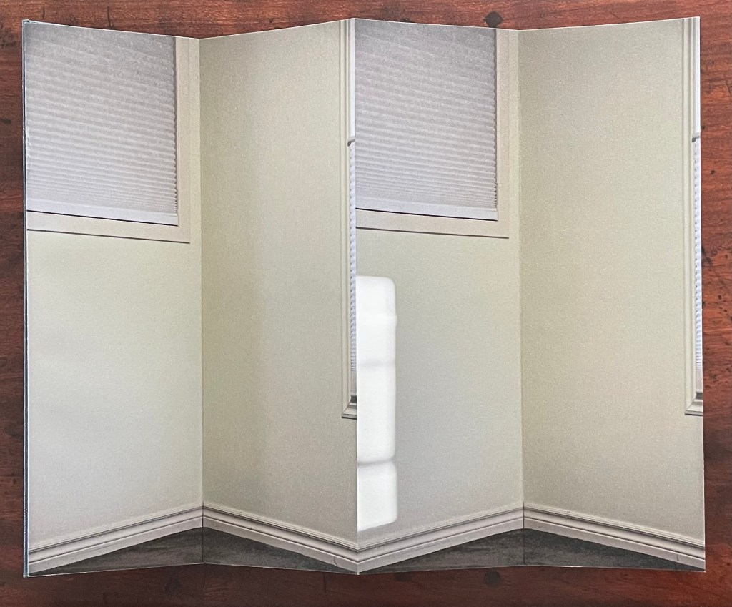 A handbound artist's book featuring a gatefold with mirrored reflections of a room's interior, showcasing a corner with a window and a light source.
