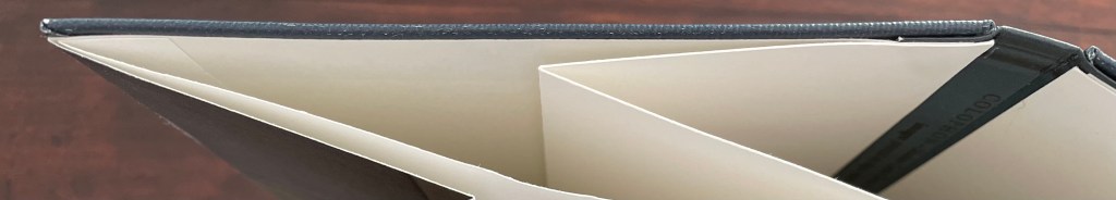 Close-up view of an artist's book with a unique accordion binding structure, showing the interior pages and the edge of the cover.