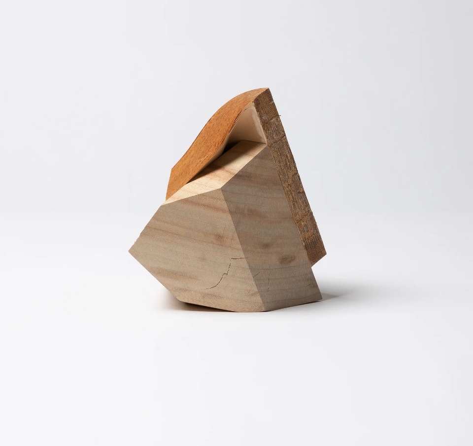 Artistic wooden sculpture resembling a geometrically abstract book, featuring angular planes and a smooth finish.