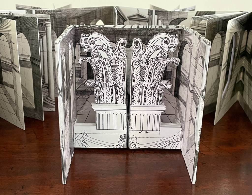 A pop-up book display featuring intricate architectural designs with columns and foliage, set against a perspective backdrop.