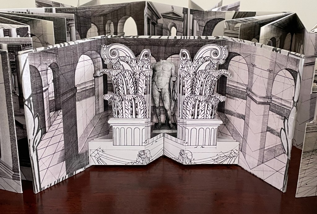 A three-dimensional pop-up book displaying intricate architectural designs with columns and a central statue.
