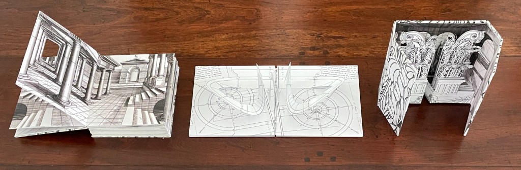 A collection of three intricately designed pop-up books featuring detailed architectural illustrations in black and white. The first book depicts a grand corridor with columns, the second contains abstract geometric shapes, and the third showcases ornate patterns and classical elements.