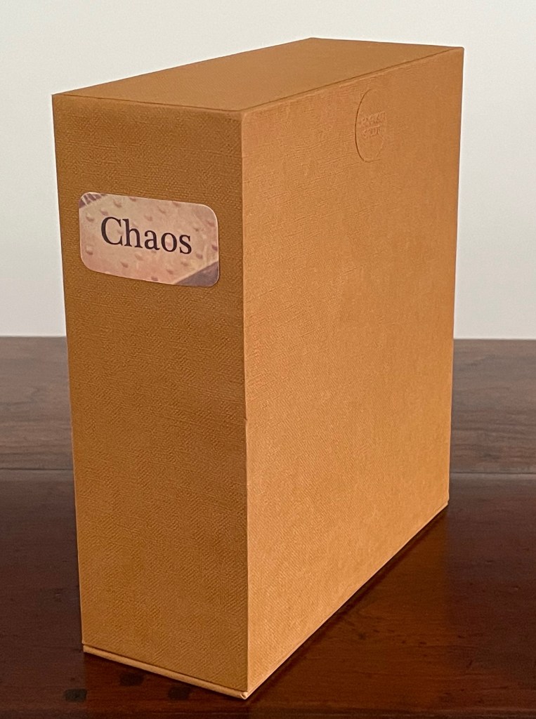 A side view of a brown box labeled 'Chaos' in a decorative font, placed on a wooden surface.