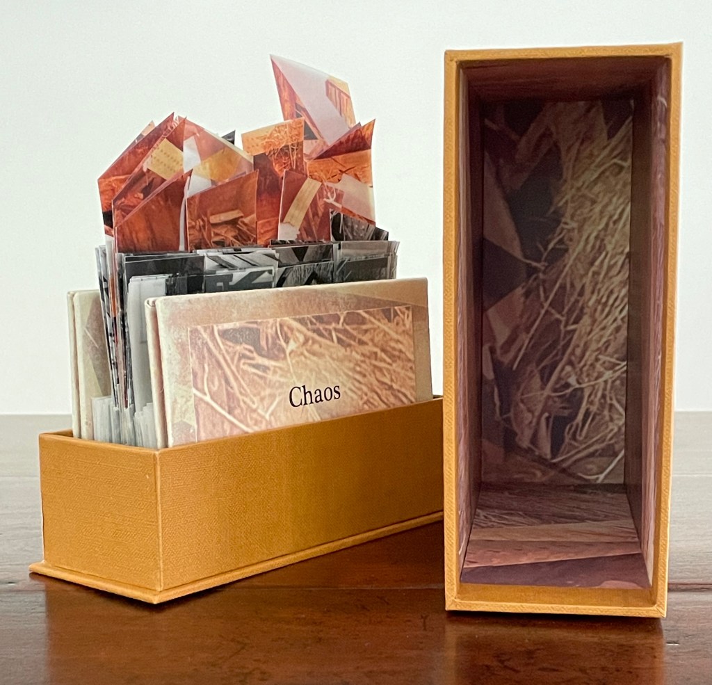 A wooden table with an orange box containing several envelopes with images inside, labeled 'Chaos.'