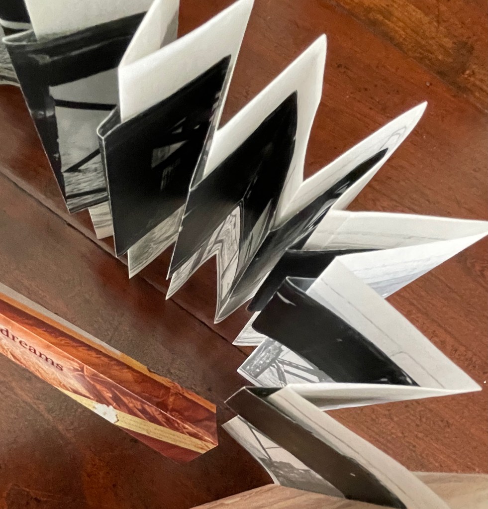 A zigzag folding photo book with black and white images, placed on a wooden surface with a hint of a title visible.