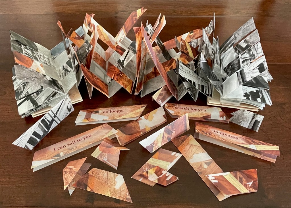 An artistic display of folded paper resembling a book or sculpture, featuring a mix of colors and textures. Surrounding the main piece are paper strips with printed phrases like 'no longer', 'I can sail to you', and 'I search for you in dreams'.