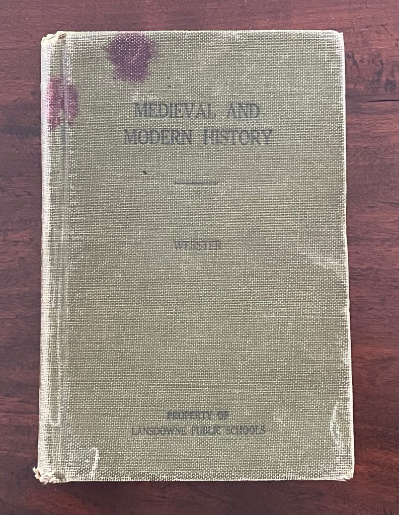 Close-up of a worn book titled 'Medieval and Modern History', showing faded text and staining on a beige spine.