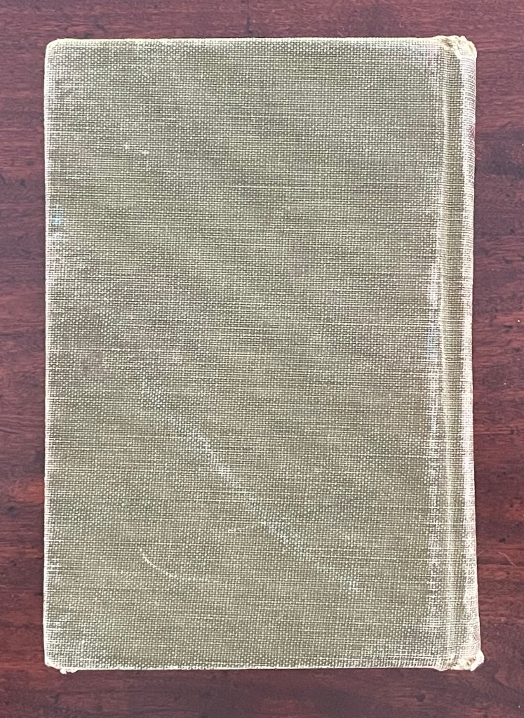 A casebound, altered hardback book with a textured green cover, resting on a wooden surface.