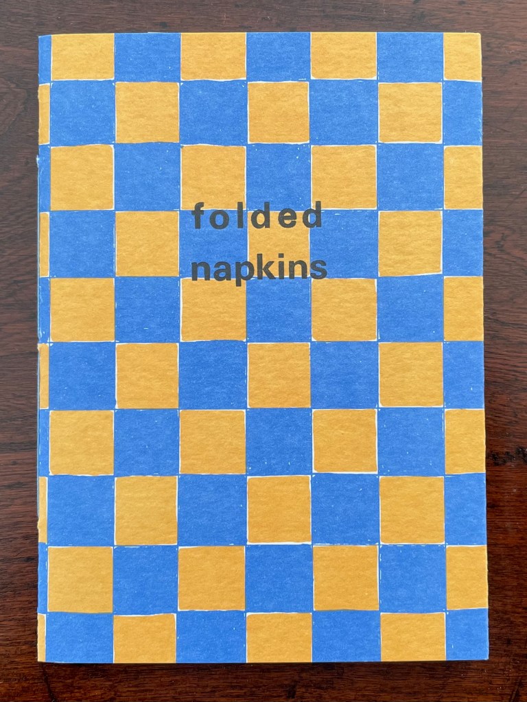 Front cover of the book 'Folded Napkins', featuring a blue and orange checkerboard pattern with the title printed in black.