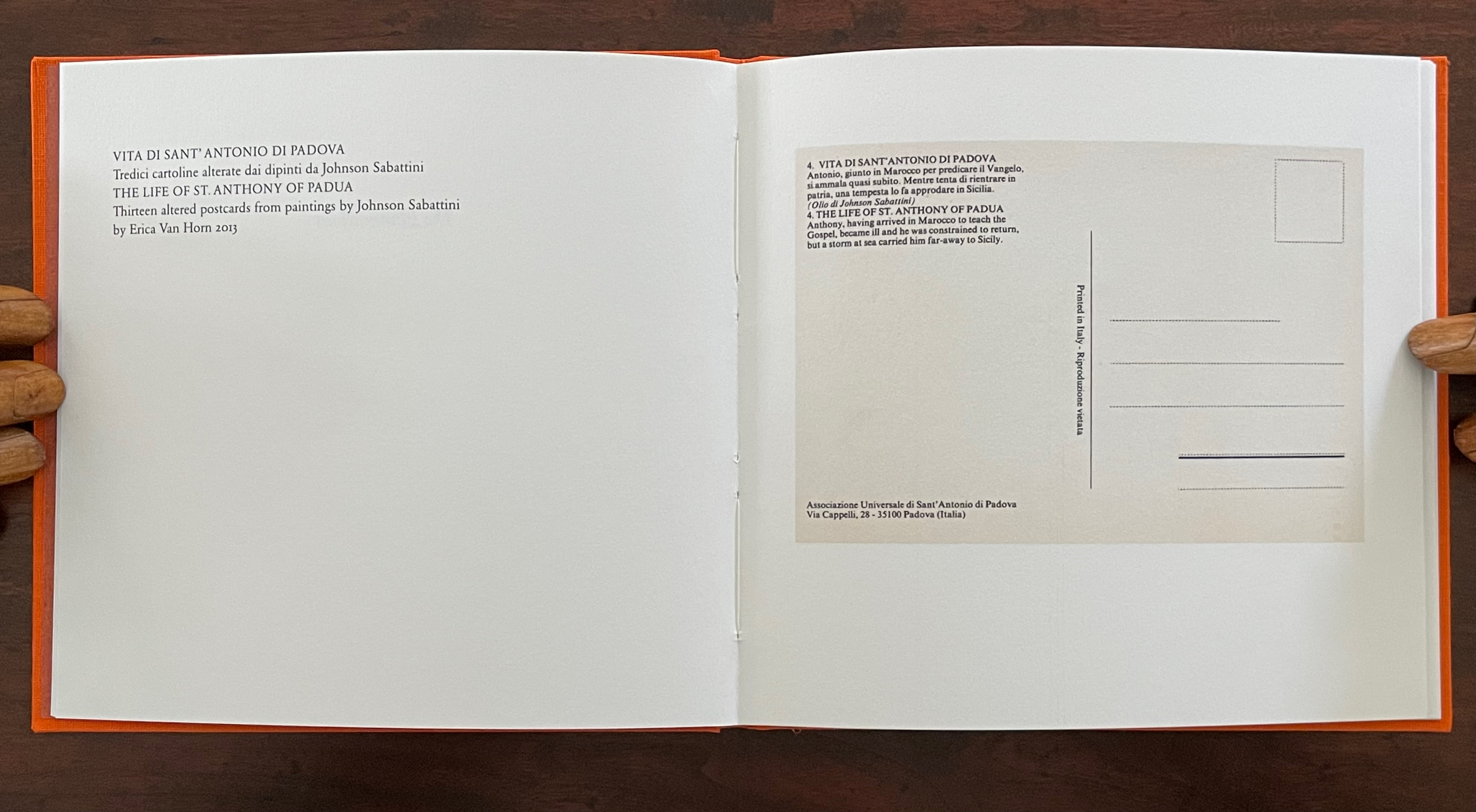 An open book displaying printed text and a blank postcard page, with hands visible at the edges, and an orange cloth cover.
