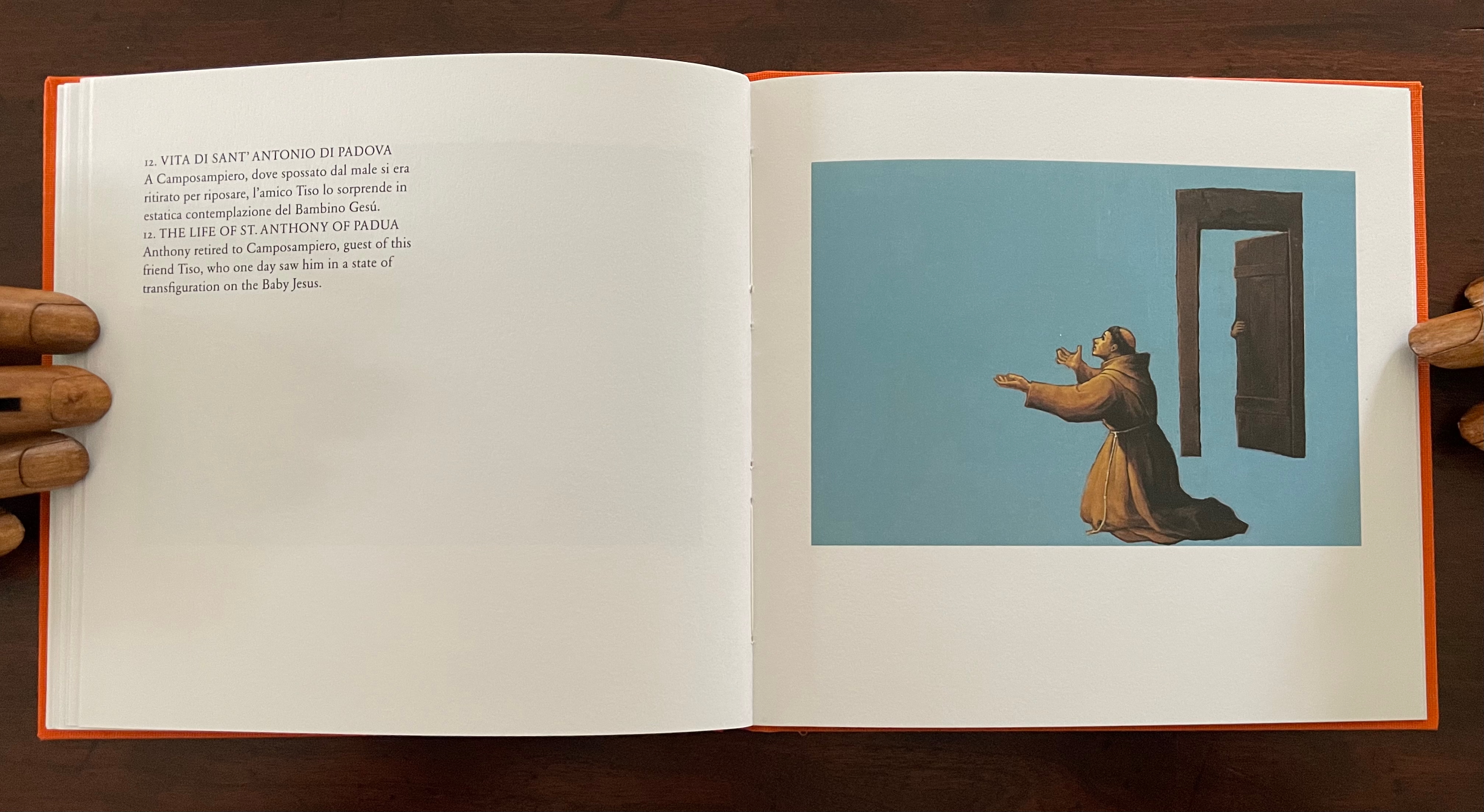 A page from a book featuring a painting of St. Anthony of Padua kneeling in prayer, with a blue background and a partially open door revealing a hand inside.