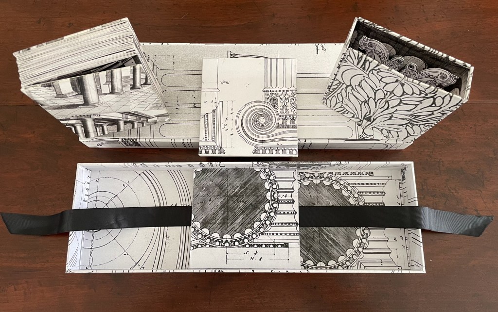 A collection of intricately designed boxes featuring architectural patterns, displayed on a wooden surface. The main box is open, revealing additional compartments and a ribbon for easy access.