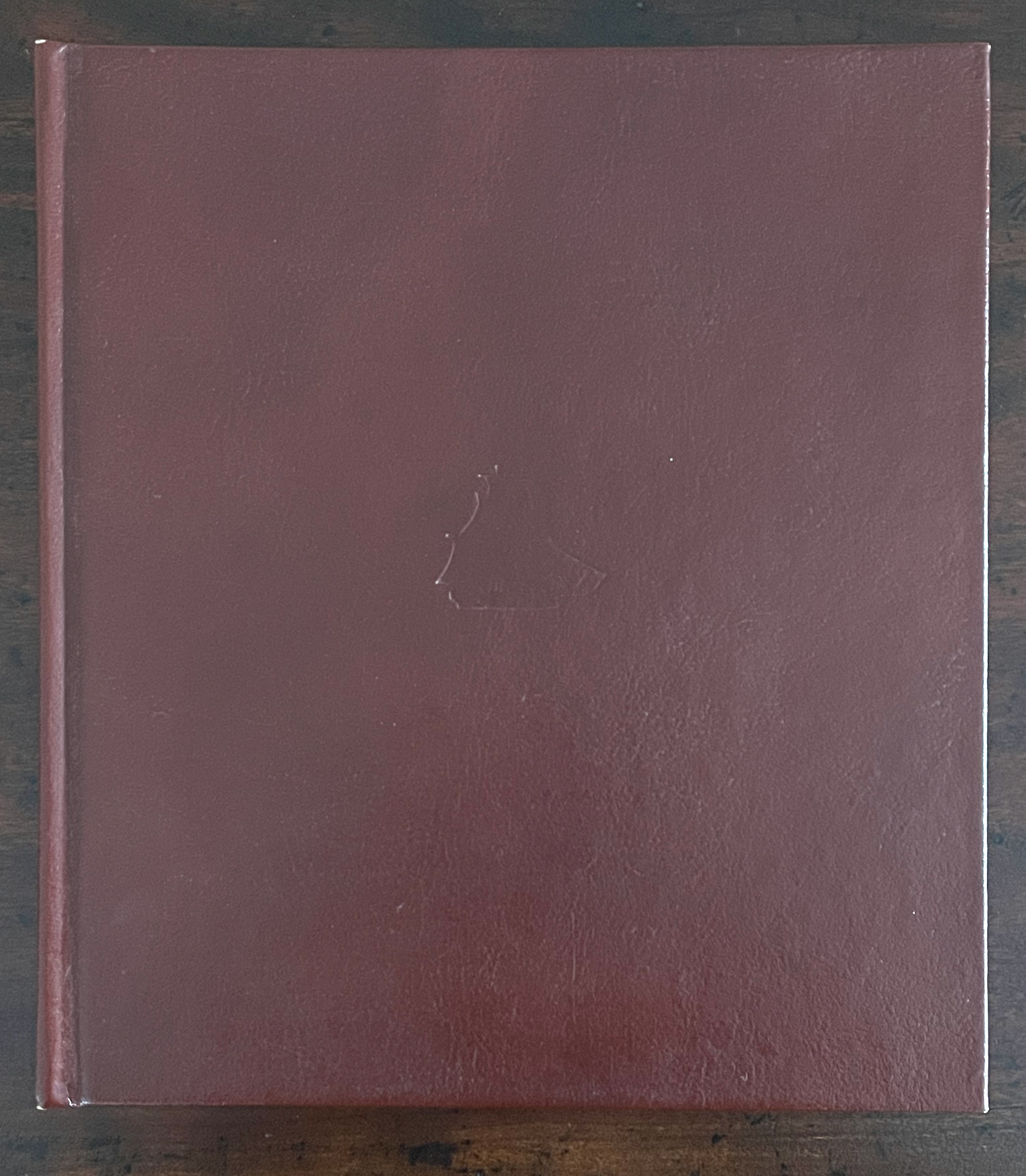 Solid maroon hardcover book lying flat on a wooden surface.