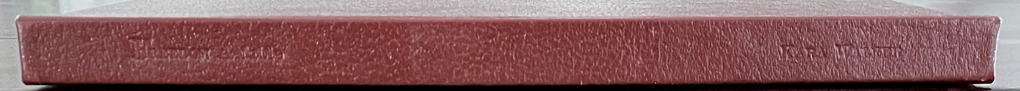 A close-up view of the spine of a thick, red-covered book with embossed lettering.