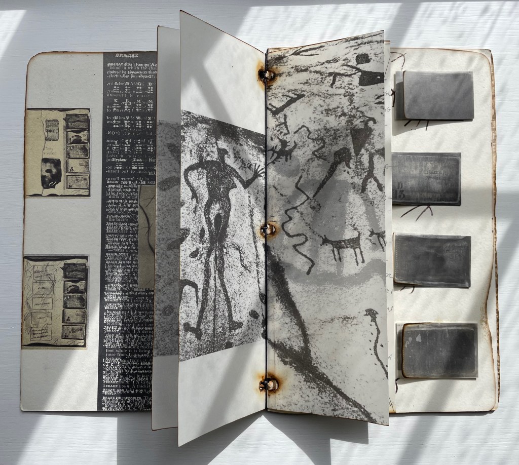 An open book displaying black and white illustrations, including ancient rock art figures and text, with several grey rectangular objects on the right page.