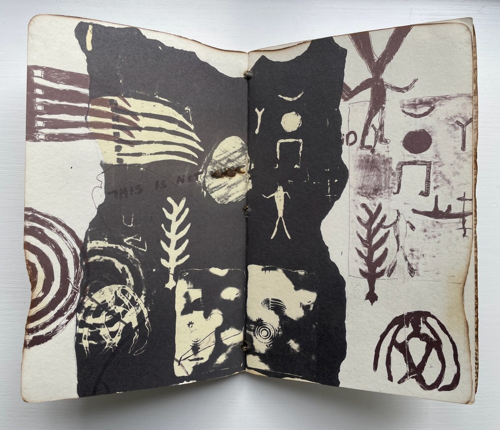 An open artist's book featuring abstract black and white drawings, including symbols, figures, and patterns, with the phrase 'THIS IS NOT LOVE' visible.