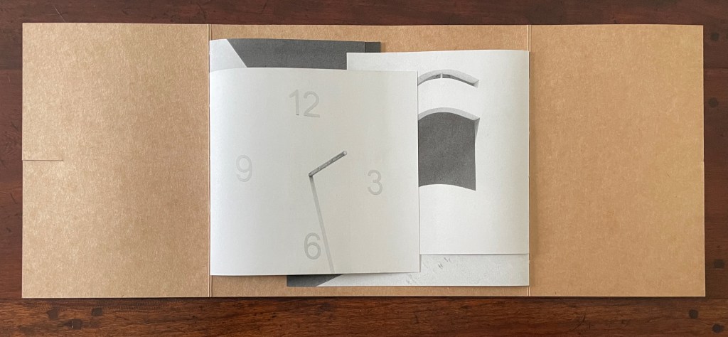 An open book or pamphlet displaying abstract graphic designs, including a clock face with minimalistic numbers and hands, set against a textured brown background.