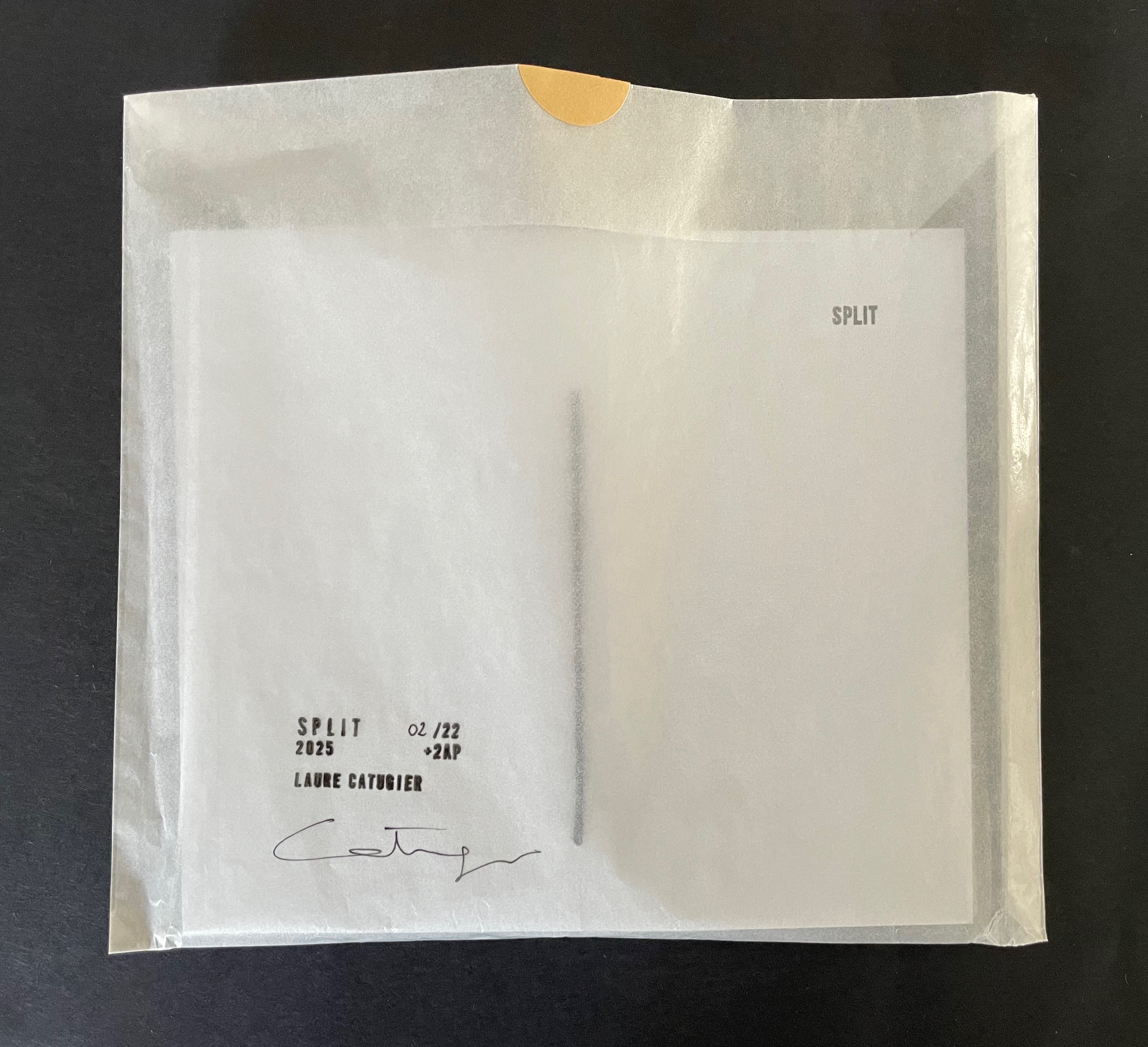 A clear plastic envelope containing a folded sheet of paper with the word 'SPLIT' printed on it, alongside markings indicating a limited edition and the name 'Laure Cattier.'