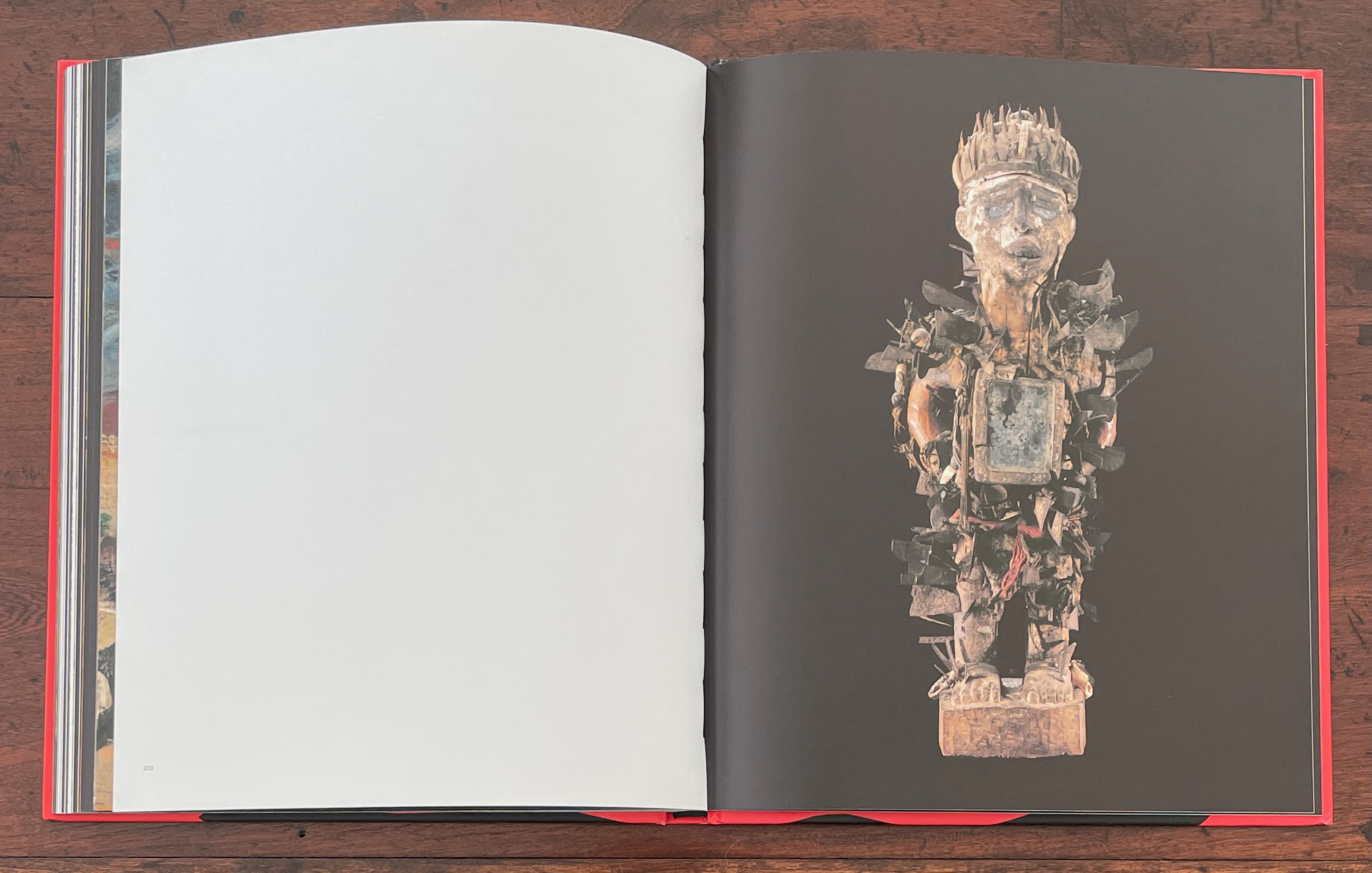 An open book displaying a page with a large, intricate statue surrounded by various elements, set against a dark background.