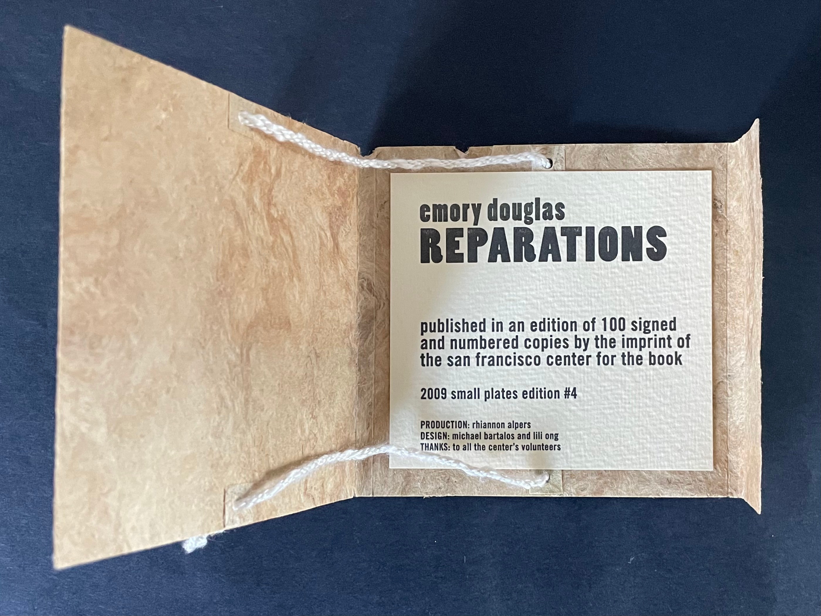 Open book with a textured cover displaying the title 'REPARATIONS' by Emory Douglas, detailing its publication and production information.