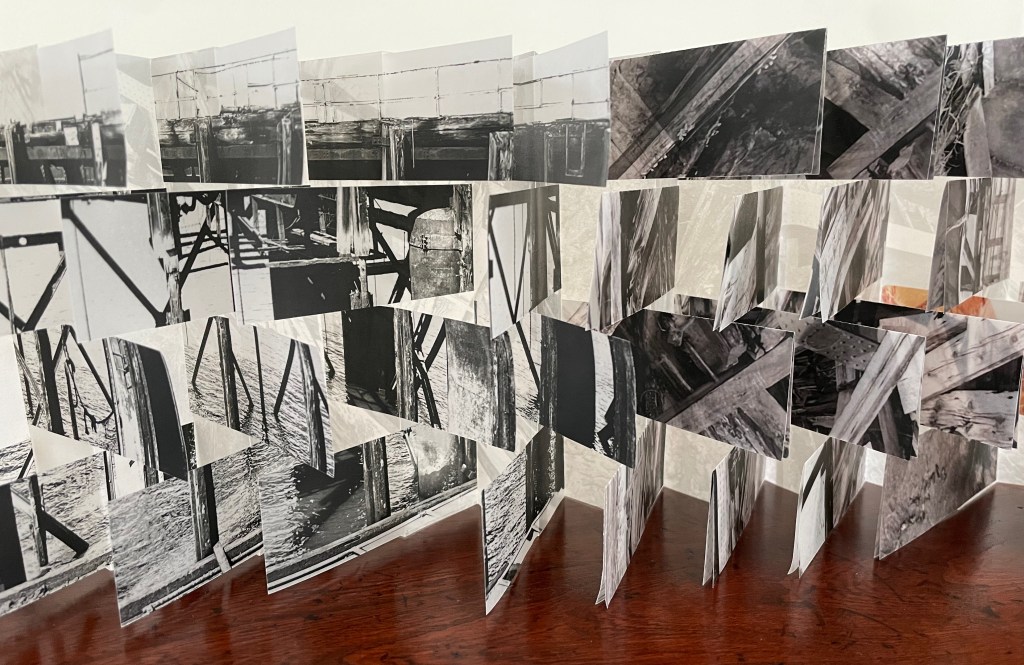 A series of black and white photographs arranged in a 3D folding structure, showcasing various views of wooden supports and structures, displayed on a wooden surface.