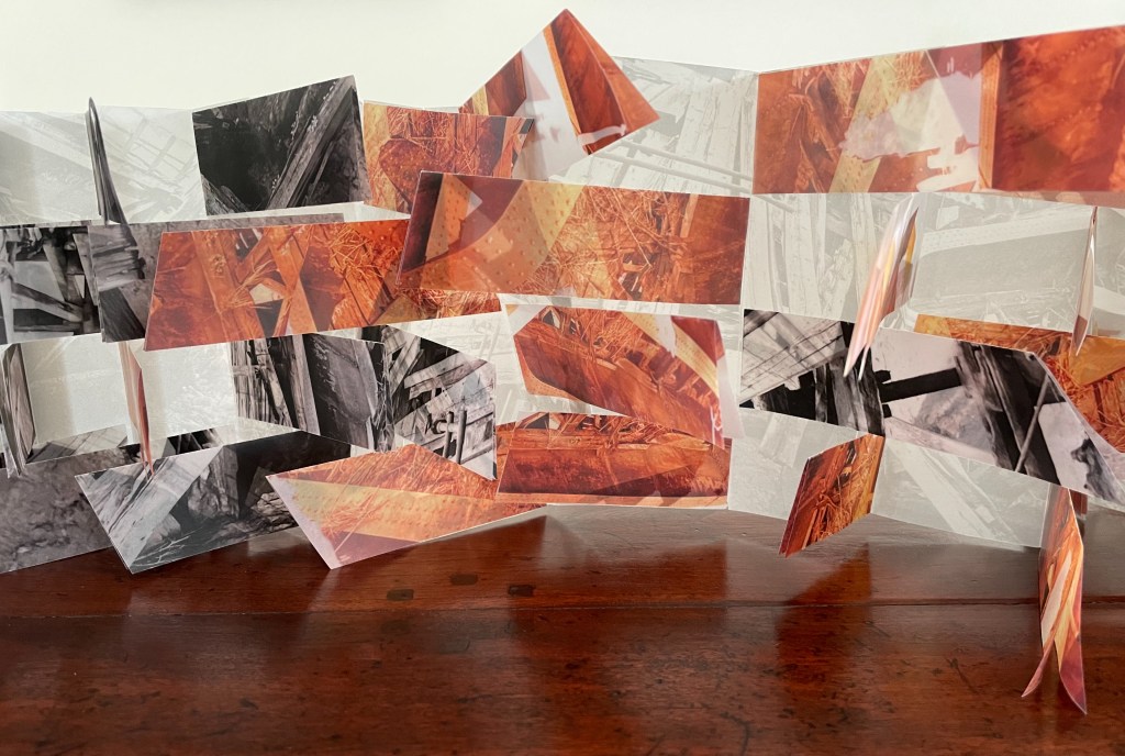 An artistic installation featuring layered paper images with abstract designs in orange, black, and white, displayed on a wooden surface.