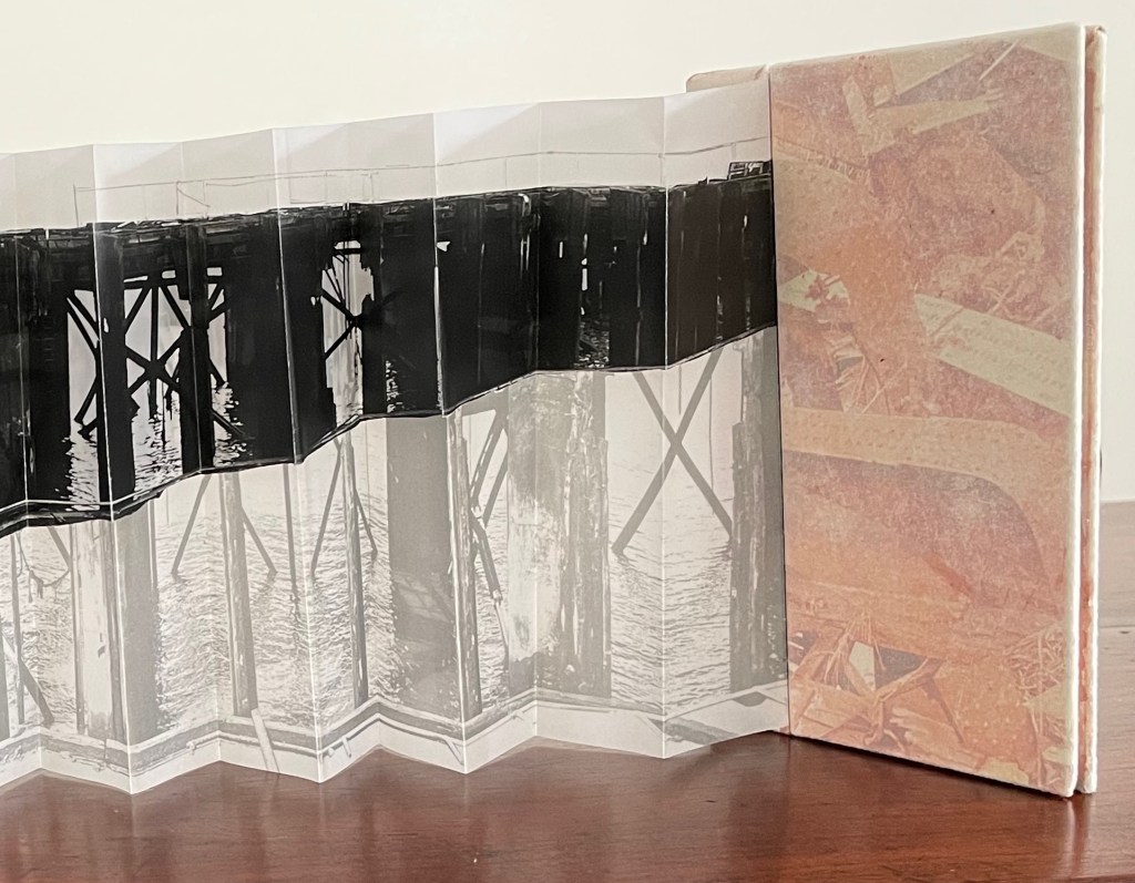 A folded book showcasing a black and white photograph of pier supports, with reflections on water, next to a textured cover with abstract colors.