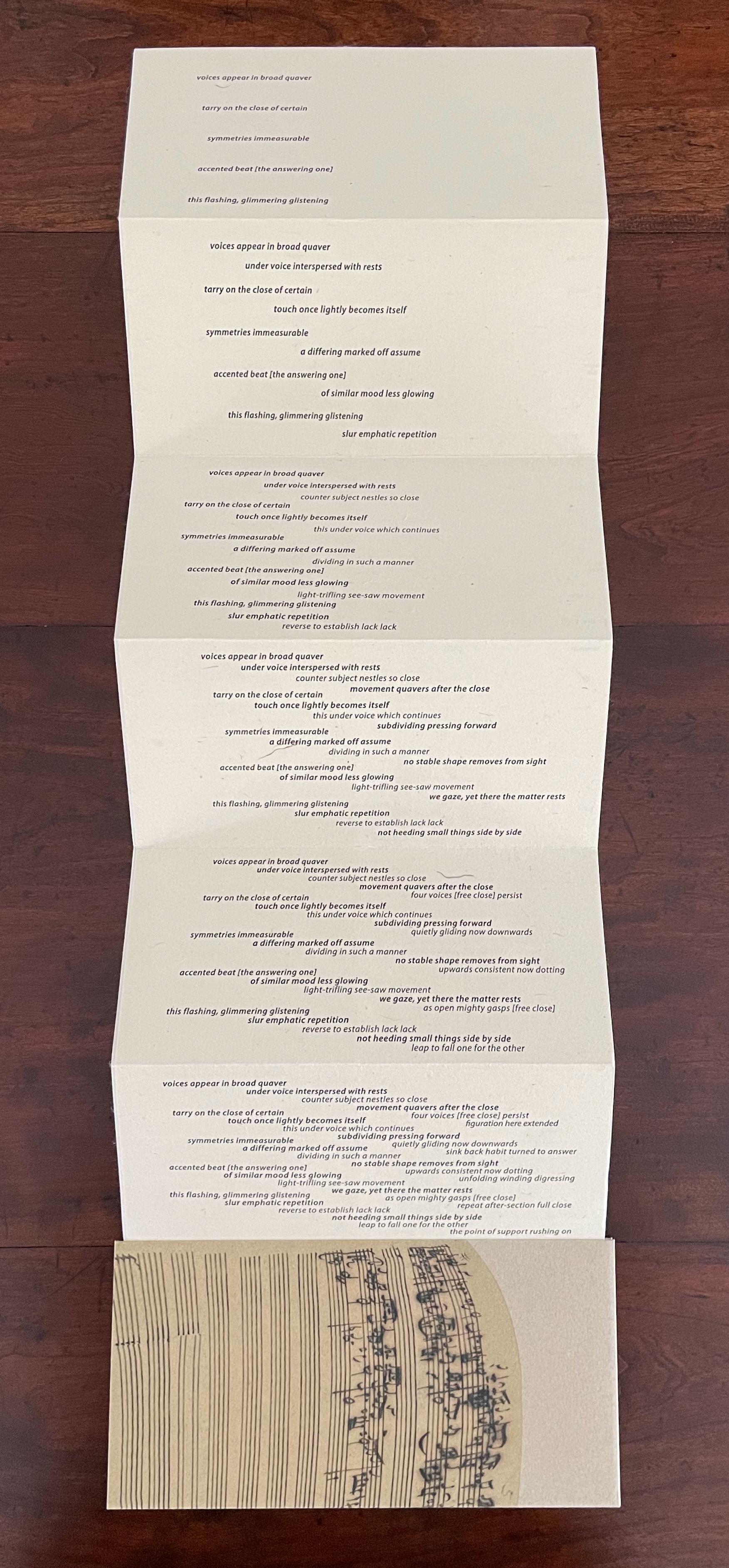 A folded piece of paper displaying a poem, with lines of text arranged in a creative format, sitting on a wooden surface. There is also a piece at the bottom that resembles sheet music.