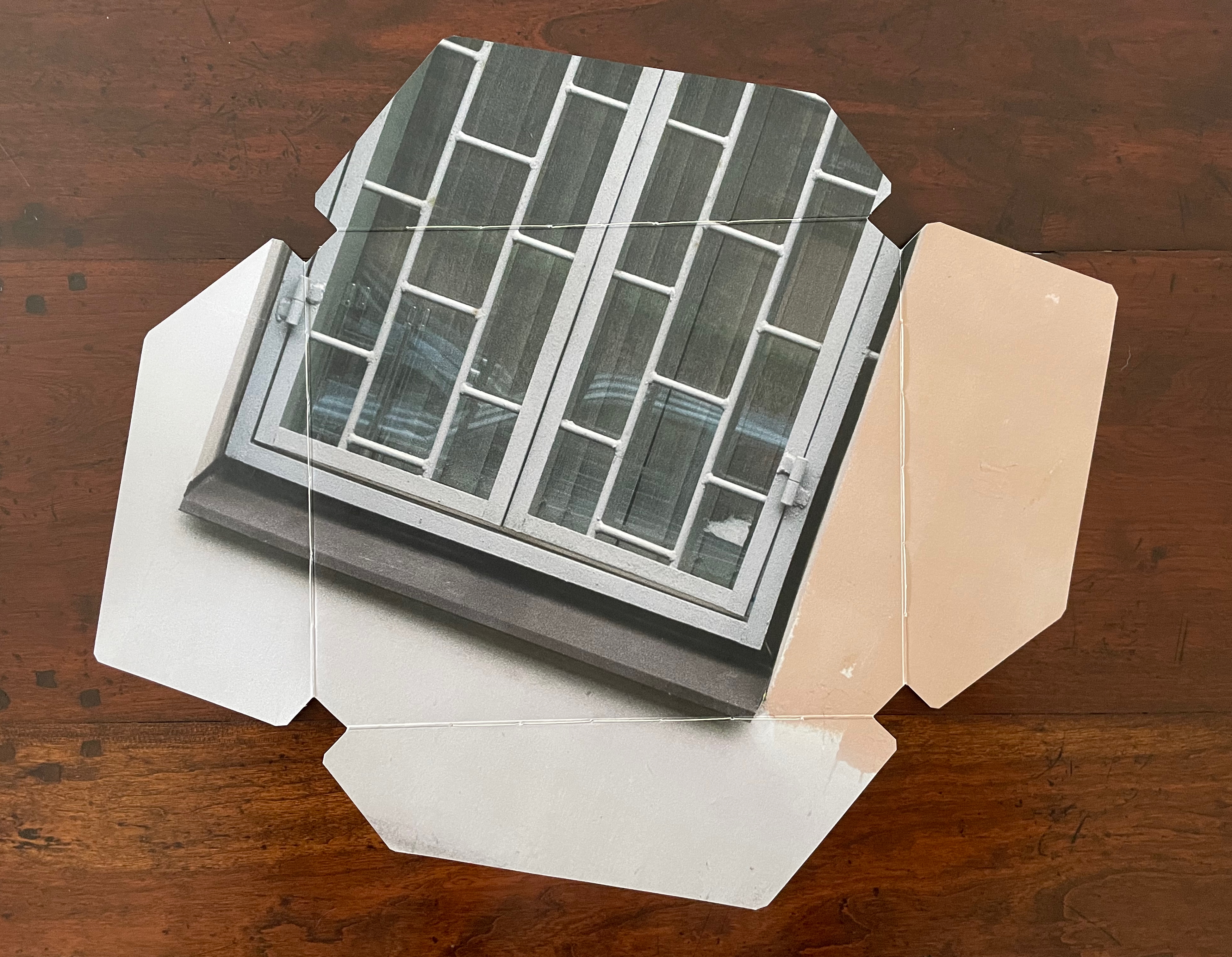 An artistic representation of a window with a grid design, printed on a flat surface resembling a fragmented paper layout.