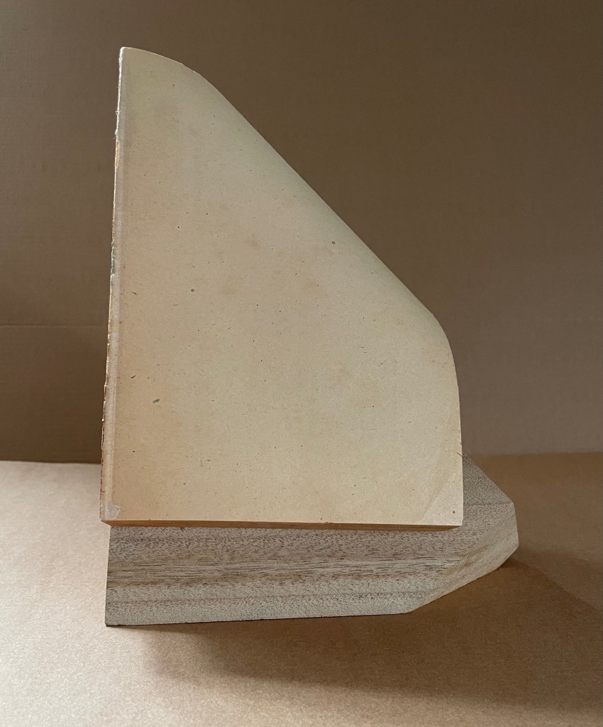 A sculptural book titled 'Silent Book, vol. 11' by Ryuta Iida, showcasing an altered book positioned on a wooden pedestal, featuring a curved cover resembling a block of camphor wood.