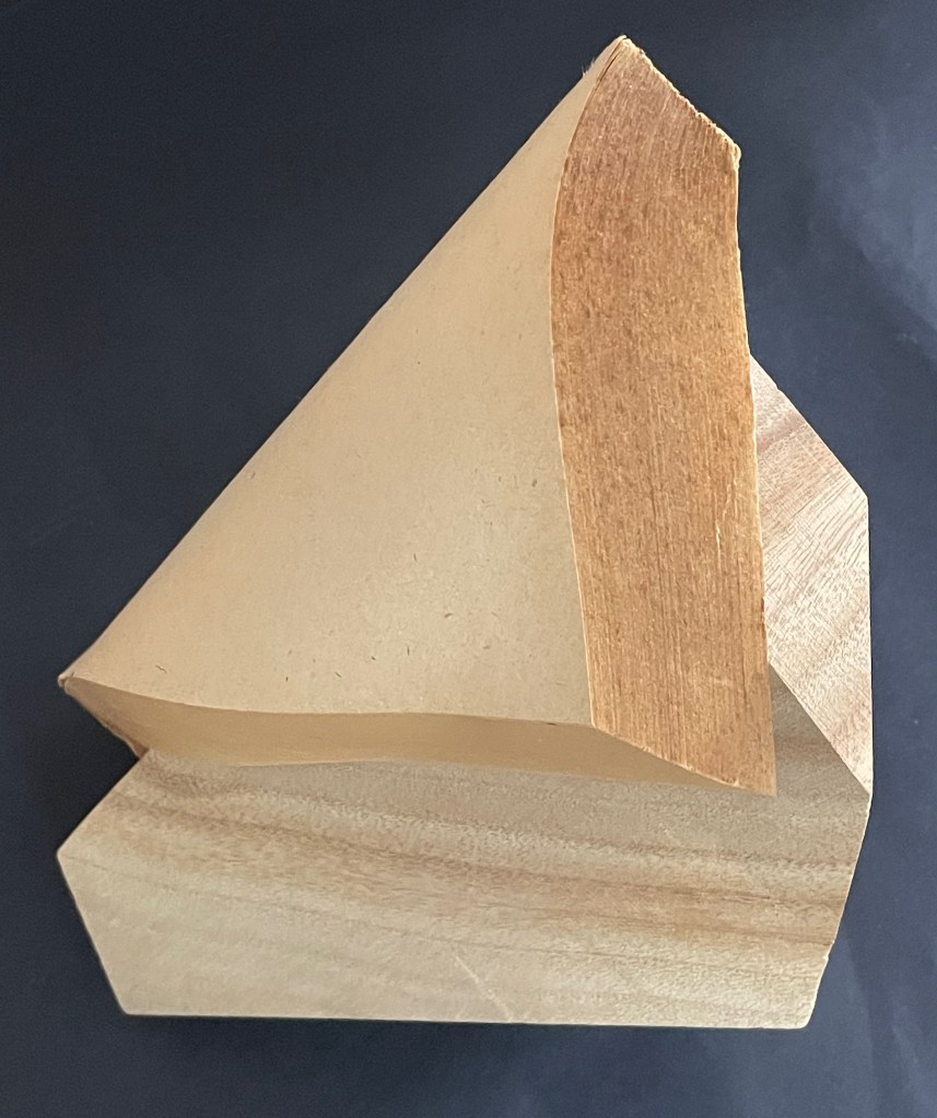 Artwork titled 'Silent Book, vol. 11' by Ryuta Iida, showcasing a sculptural composition of a camphor wood block and paper, featuring angular shapes and layered textures.