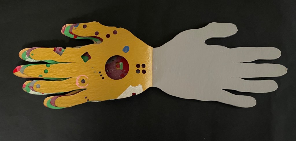 A stylized hand sculpture featuring a colorful, patterned palm on one side and a plain gray back on a black background.