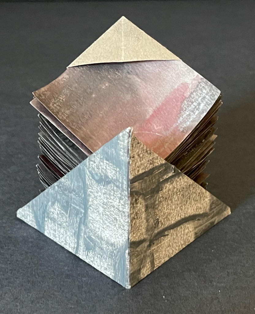 A stack of triangular pyramids made of textured cards, displaying different colors and patterns, set against a dark background.
