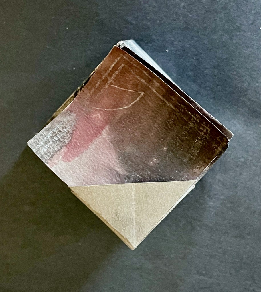 A small, folded piece of paper or booklet with a textured surface, resting on a dark background.